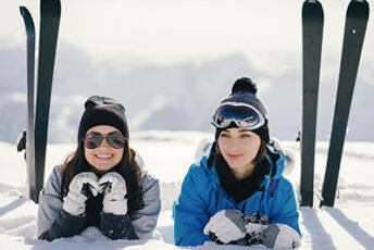 two young and active brunette sitting in the snowy mountains with ski